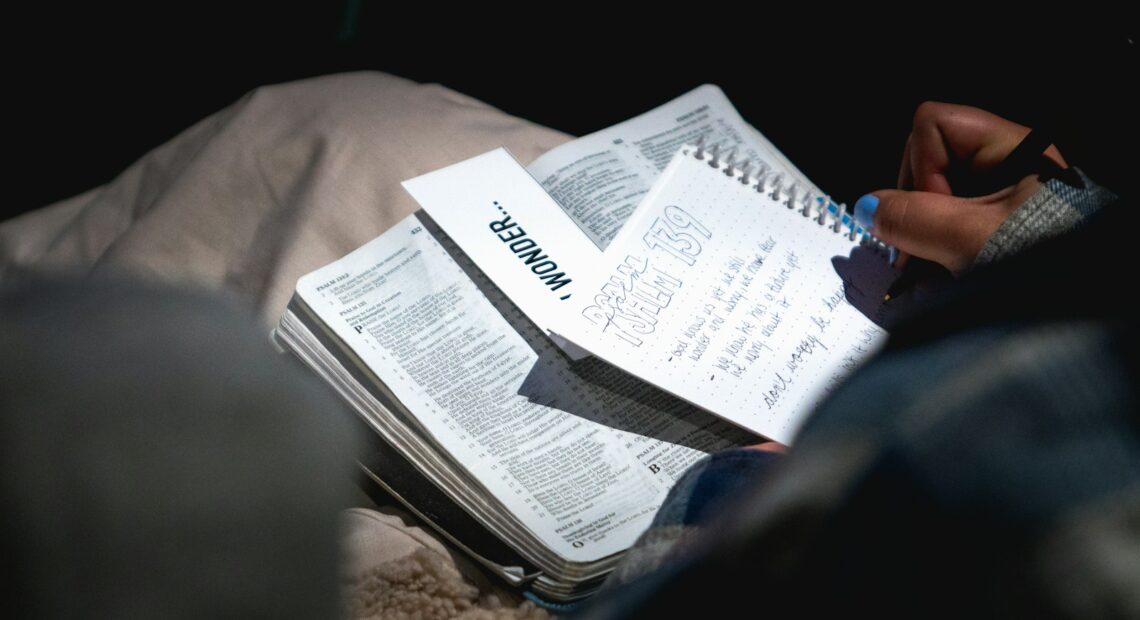 person holding black pen and writing on white notebook
