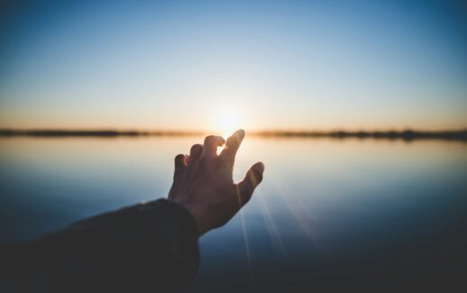 landscape photography of person's hand in front of sun